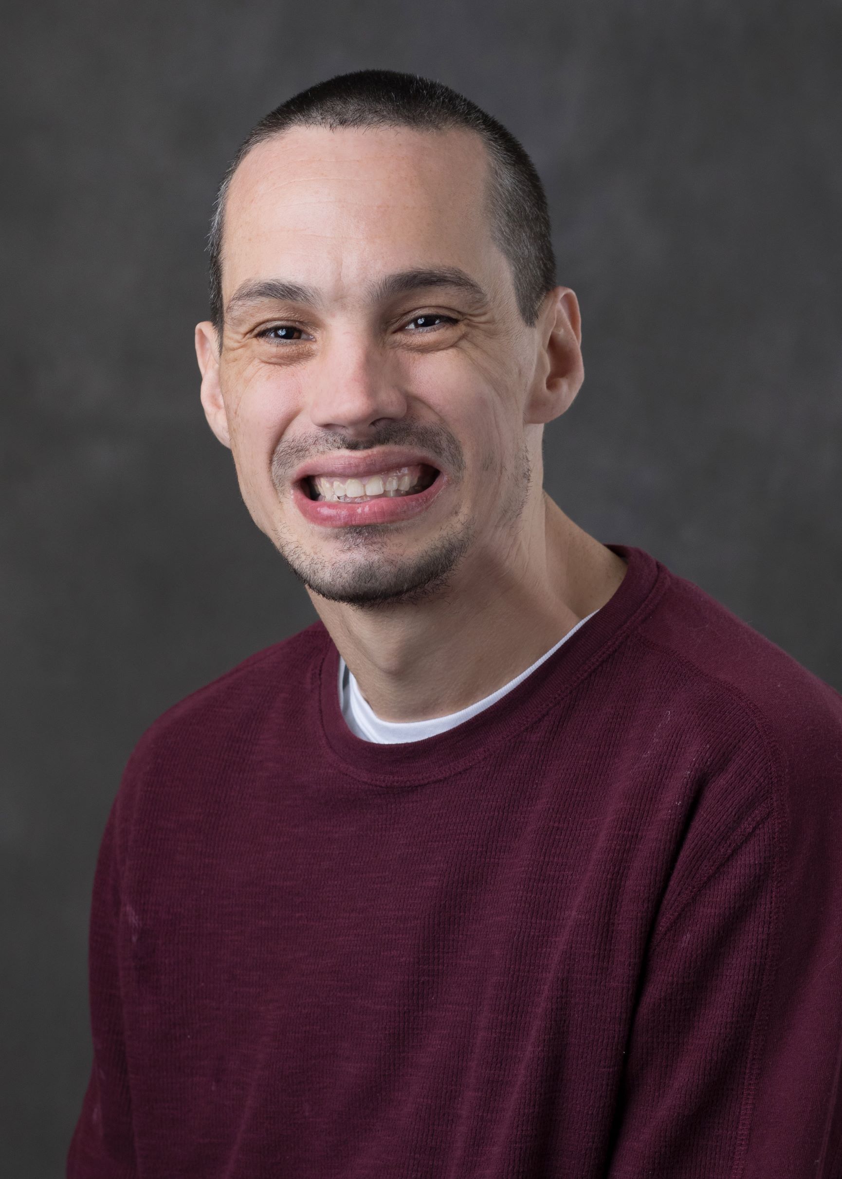 A professional portrait of man with short hair and a red sweater smiling at the camera