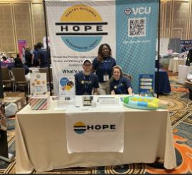 Picture of three people standing behind an exhibit hall table for the Hope Lab